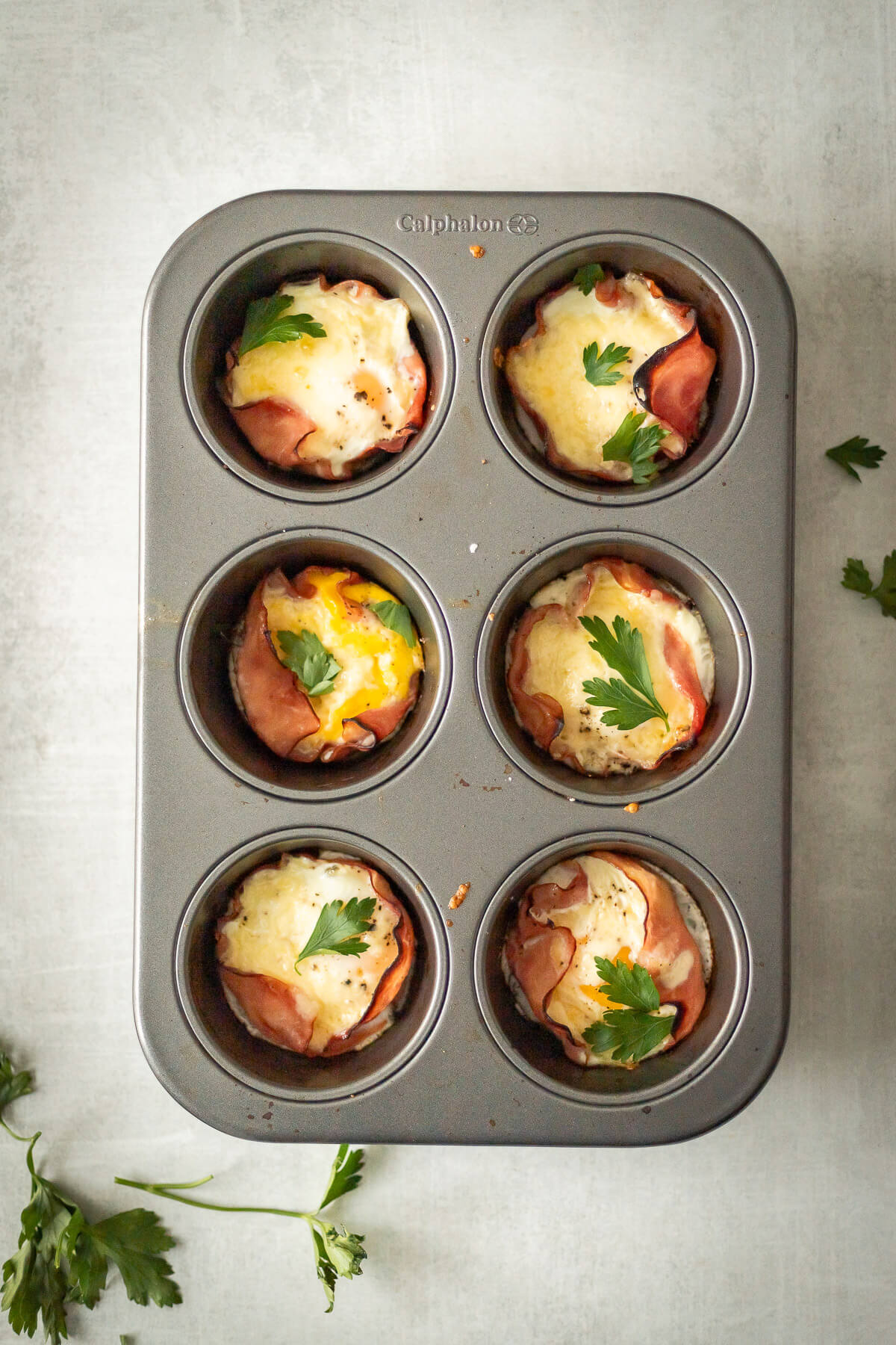 Baked Ham and Egg Cups with Shredded Cheese in a muffin tin, topped with fresh parsley