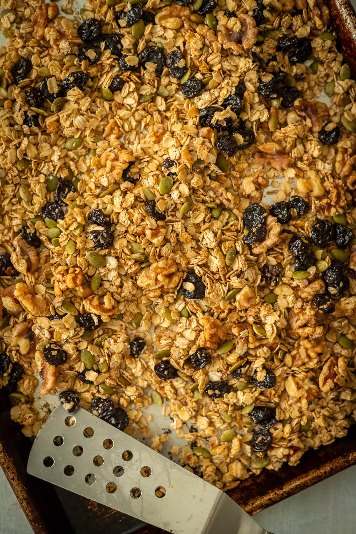 cherry walnut granola on a sheet pan with a spatula